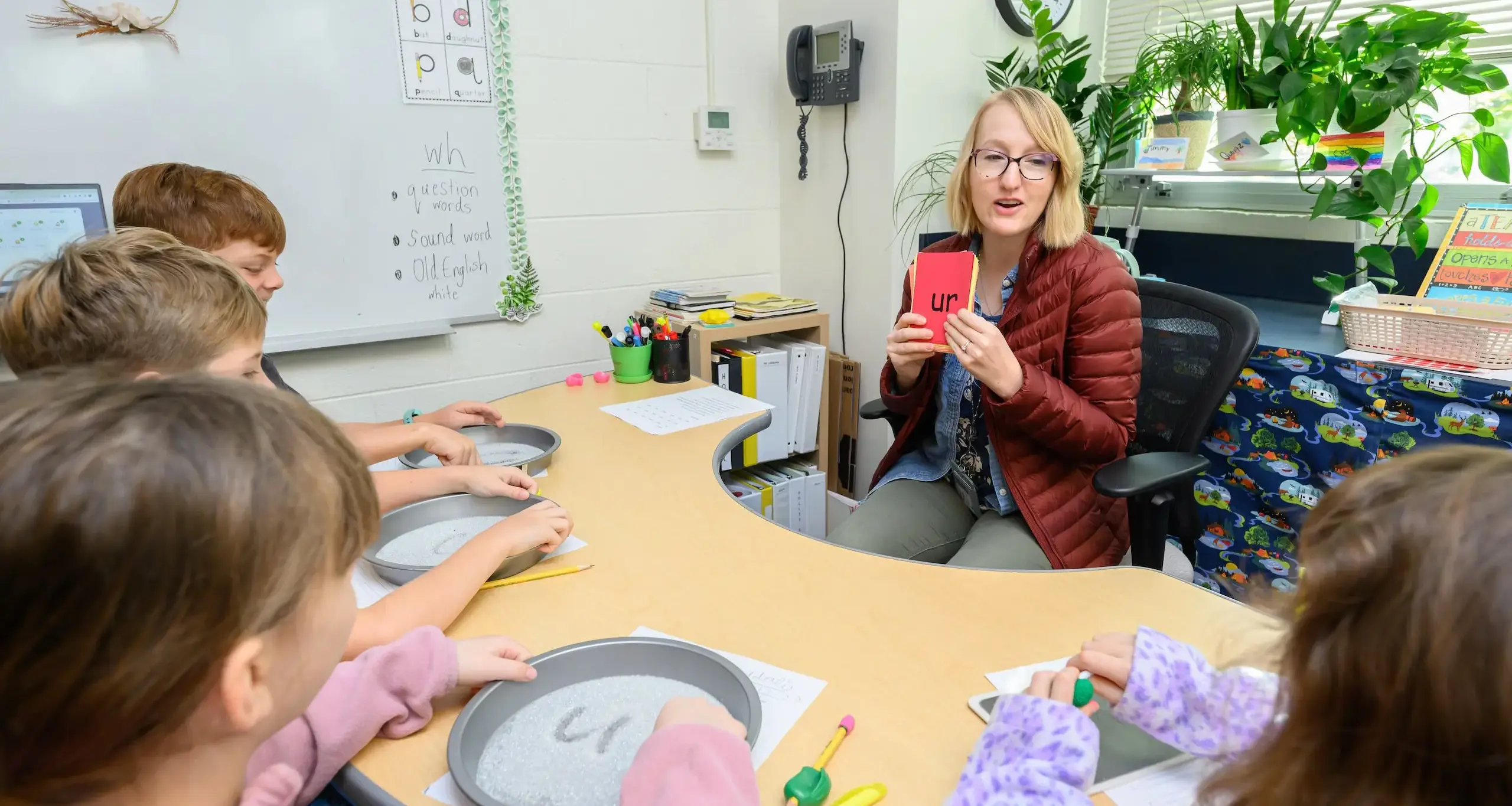 Walker teacher holding phonetics card and sitting in a table with walker students in a class